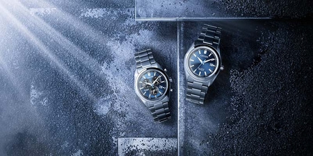 Twee Citizen horloges met blauwe wijzerplaten op een getextureerd donker oppervlak.