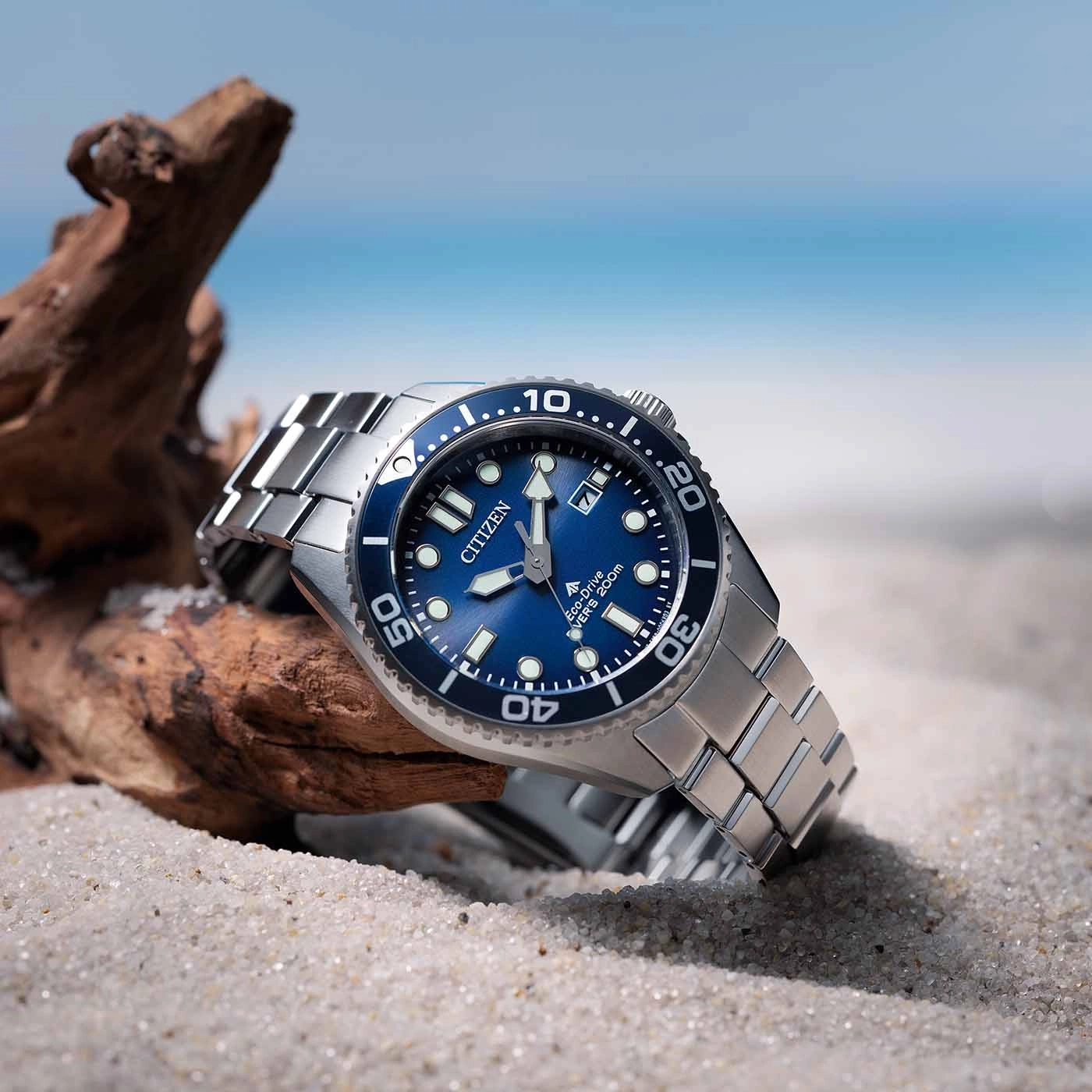 Citizen horloge op zand met blauwe wijzerplaat en oceaan achtergrond