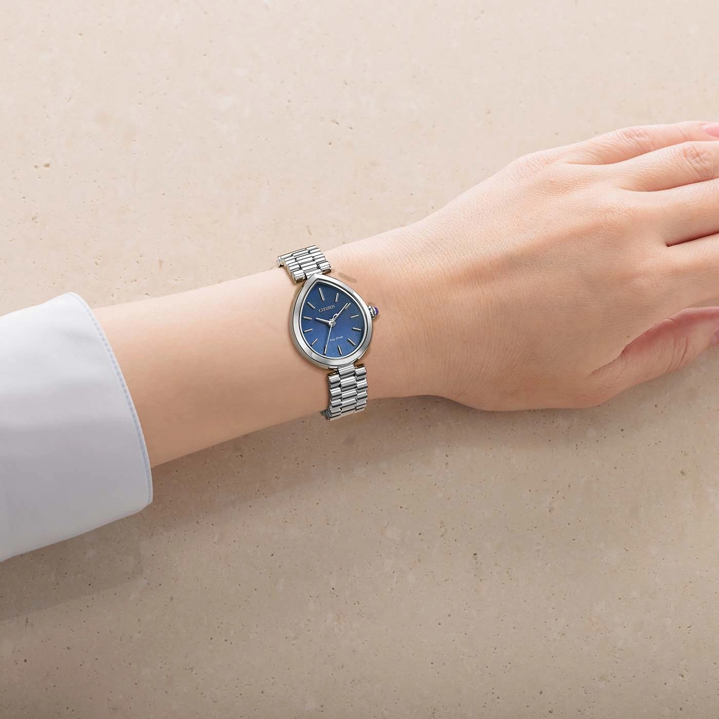 De pols van een vrouw draagt een zilveren horloge met een blauwe wijzerplaat.