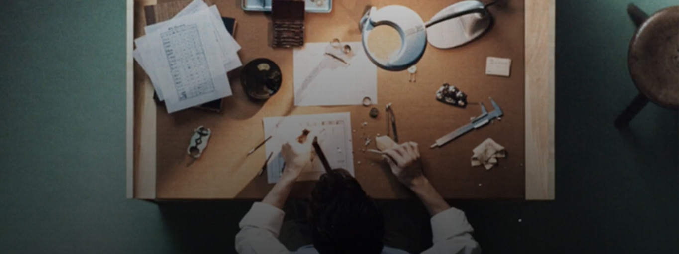 Juwelier aan het werk, sieraden maken op een houten bureau met gereedschap en papieren.
