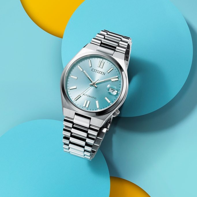 Citizen horloge met lichtblauwe wijzerplaat op kleurrijke achtergrond.
