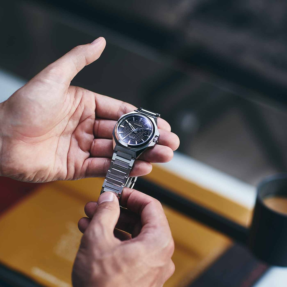 Close-up van een persoon die een Citizen-horloge met een zwarte wijzerplaat vasthoudt.