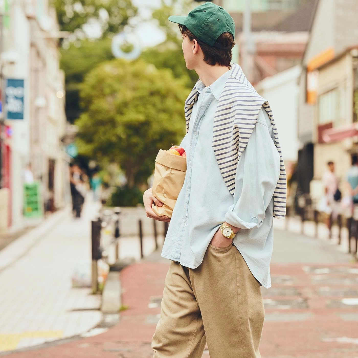 Een man met een pet en lichtblauw shirt loopt een straat in en draagt boodschappen.