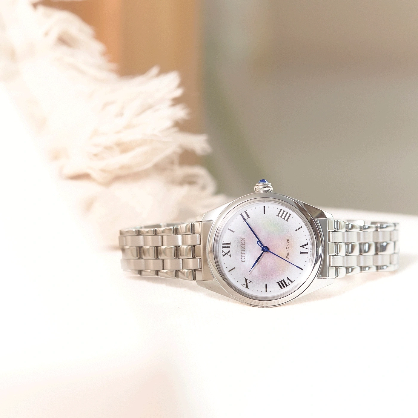 Citizen horloge met witte wijzerplaat en zilveren band op een wit oppervlak.