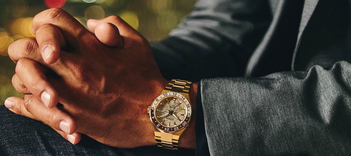 Man met gouden horloge, handen gevouwen, jasje, bokeh achtergrond.