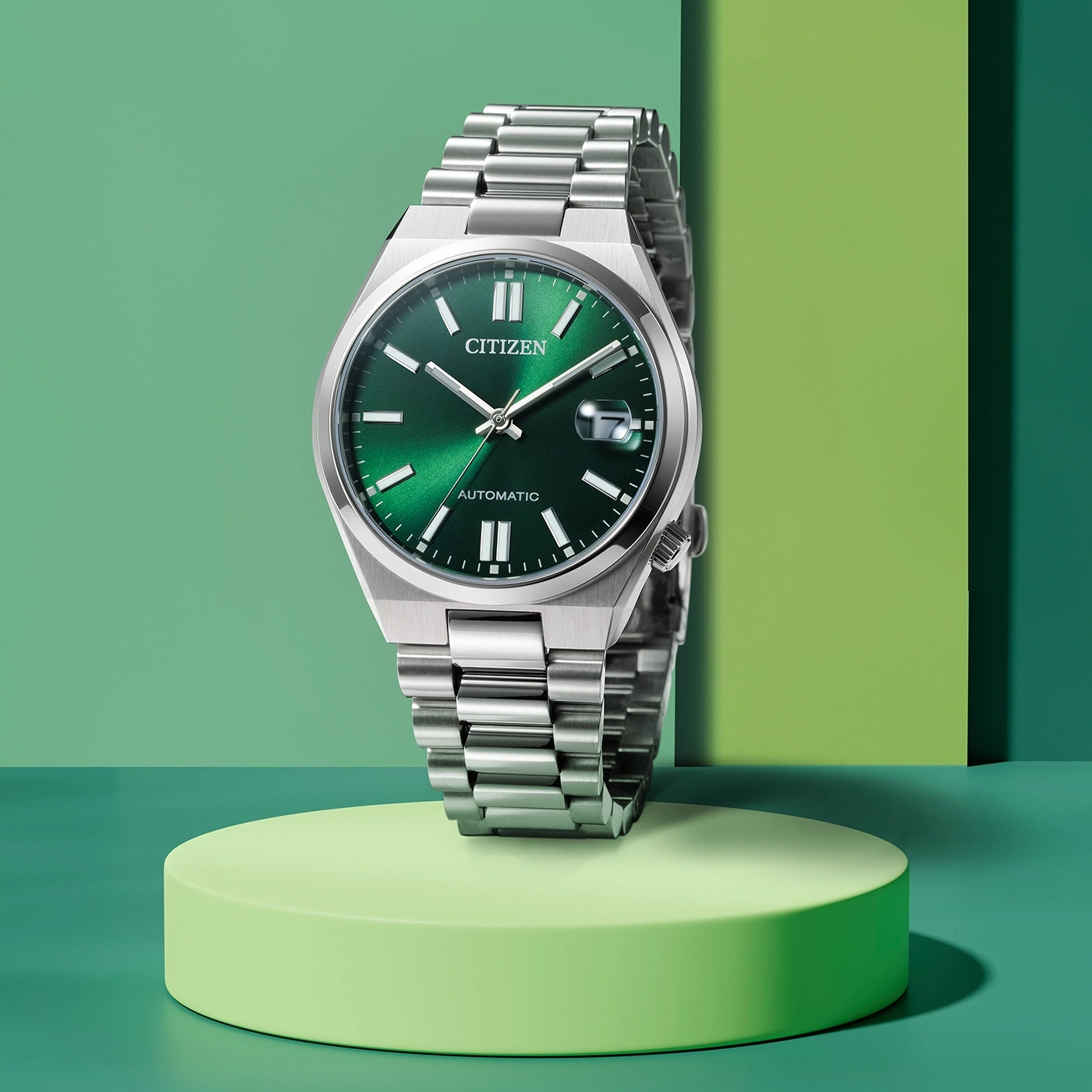 Citizen horloge met groene wijzerplaat en zilveren band op groen platform.