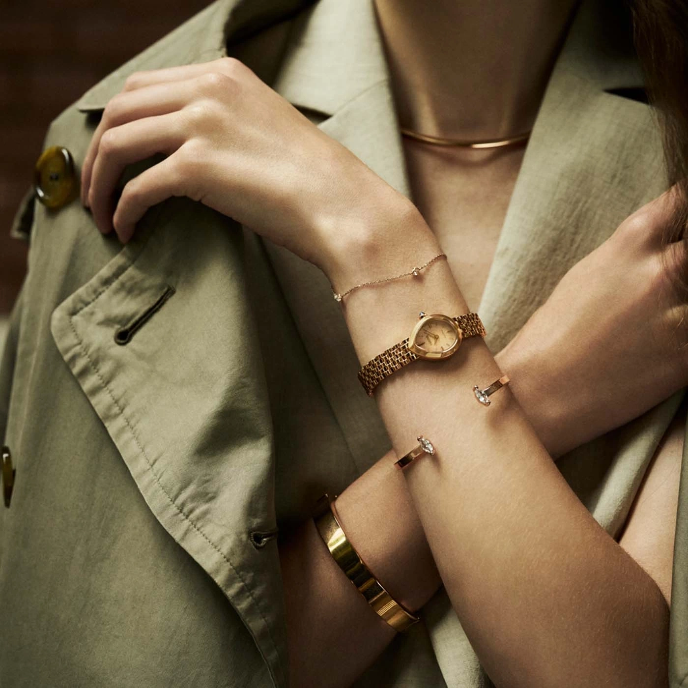 Close-up van de armen van een vrouw versierd met gouden sieraden, waaronder een horloge en armbanden.