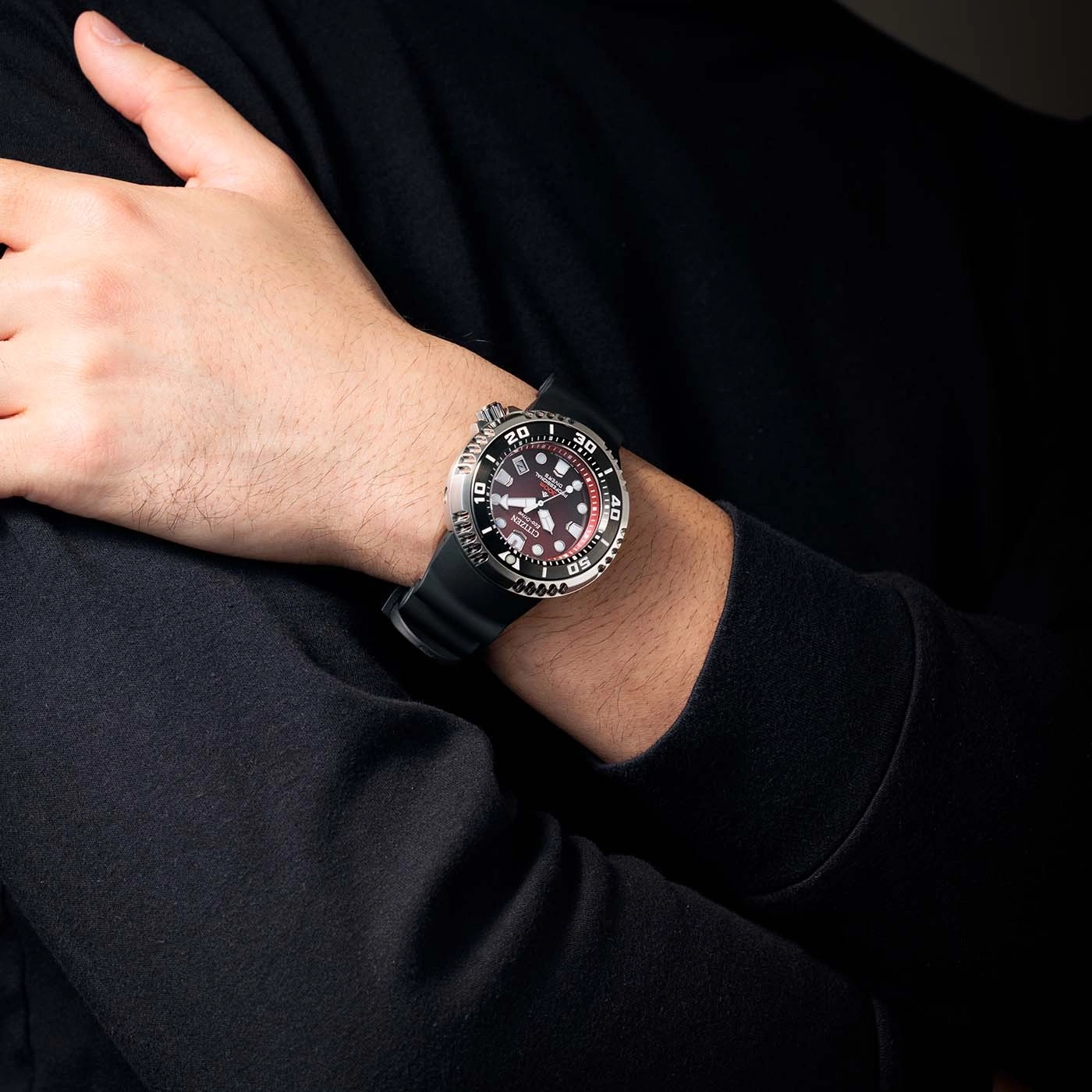 Man draagt Citizen horloge met zwarte band en rode wijzerplaat.
