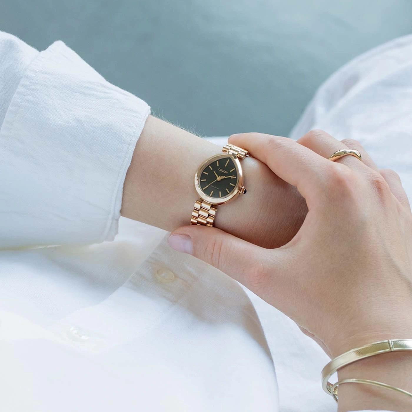 Een vrouw met een gouden horloge en armband, die haar gezicht aanraakt.
