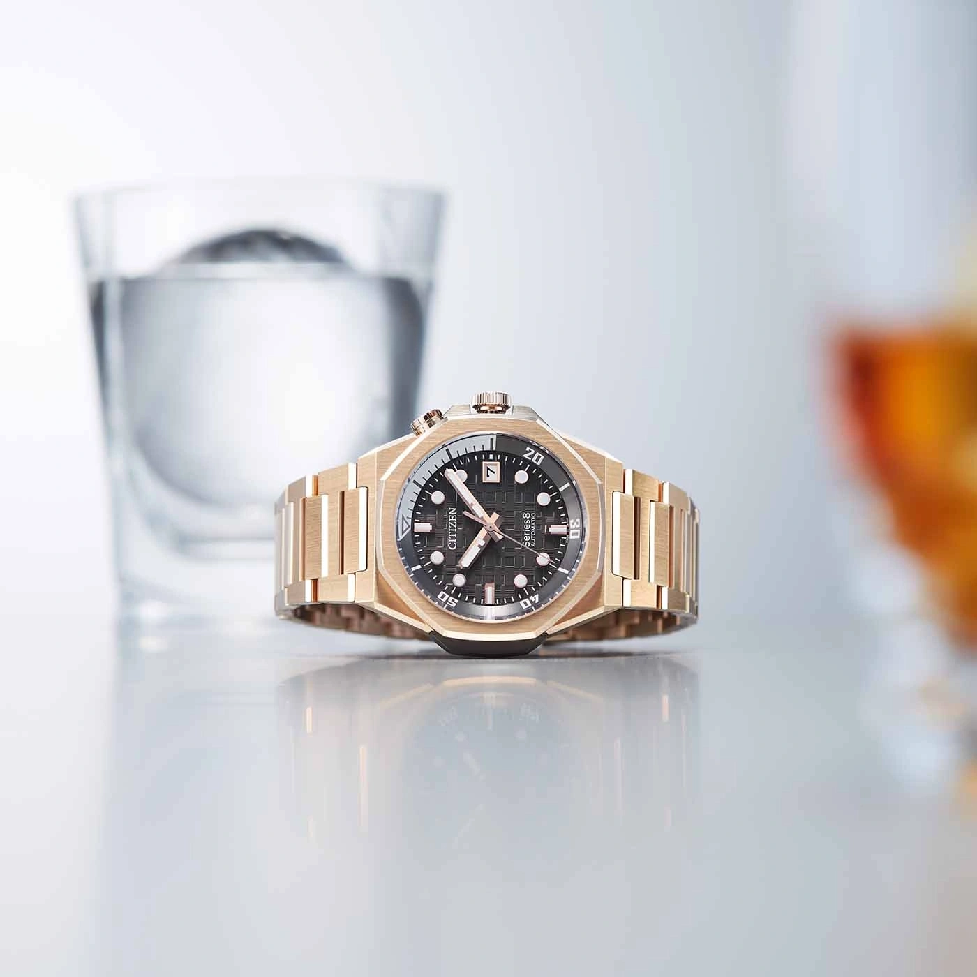Gouden horloge met zwarte wijzerplaat, glas water en reflecterend oppervlak.
