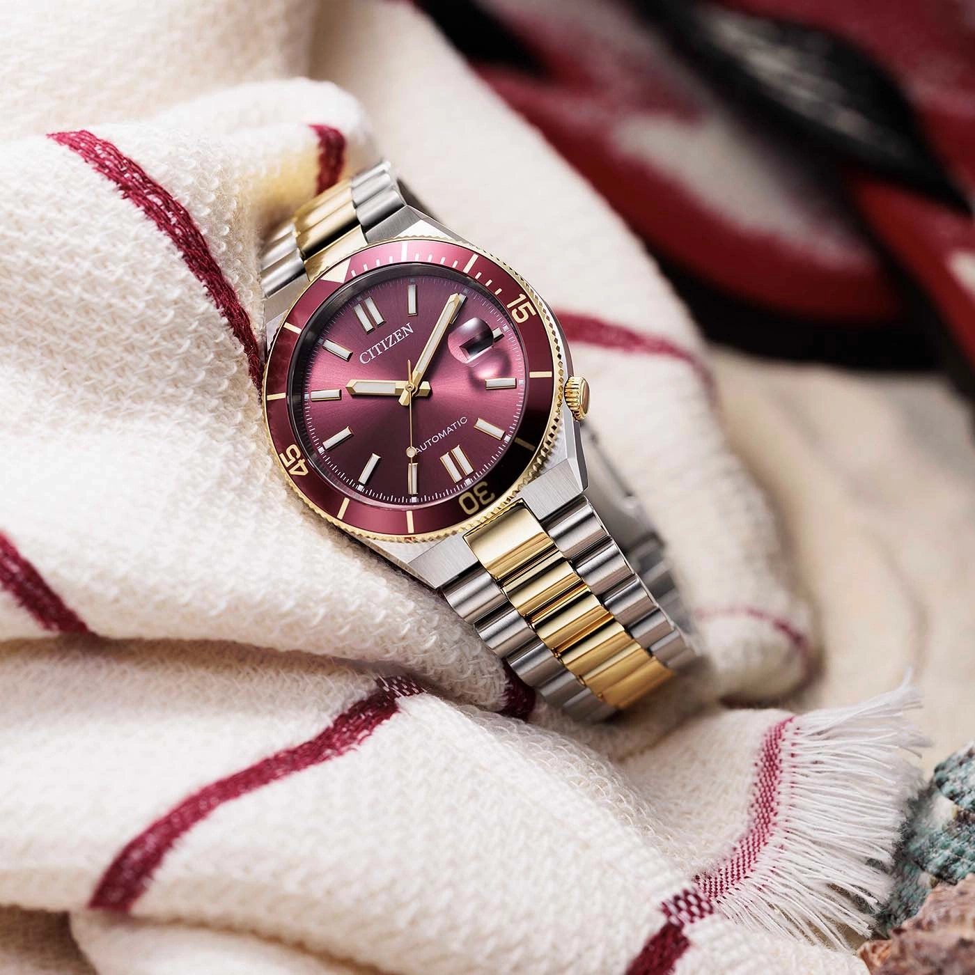 Close-up van een Citizen automatisch horloge met een rood wijzerplaat en gouden accenten.
