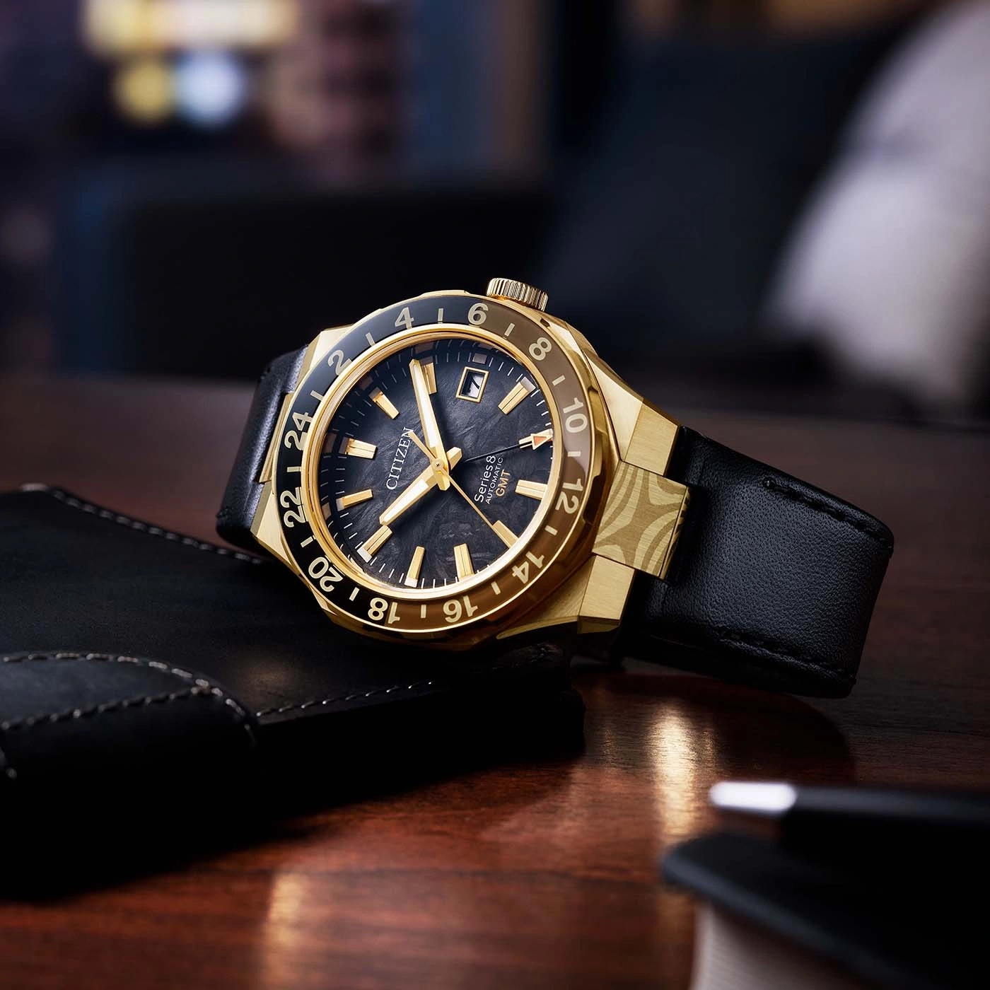 Een gouden Citizen GMT horloge met zwarte wijzerplaat en leren band.
