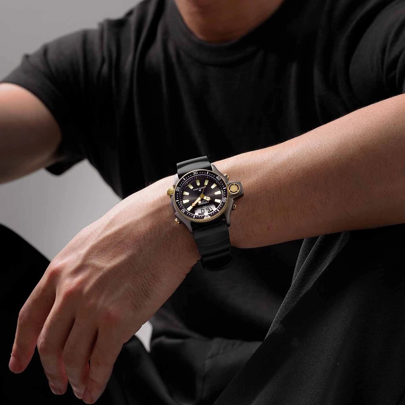 Man draagt een zwart horloge met een zwarte band en gouden accenten.