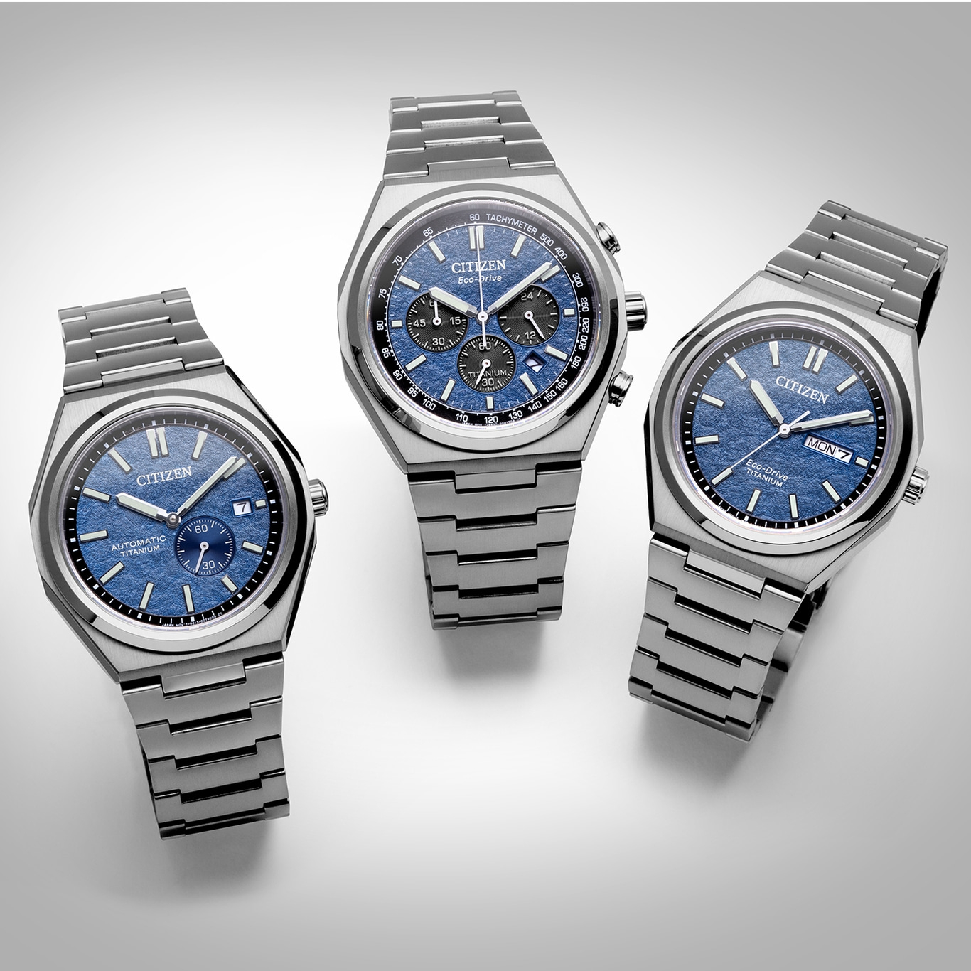 Drie Citizen horloges met blauwe wijzerplaten en titanium banden op een witte ondergrond.
