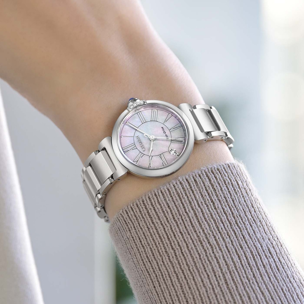 De pols van een vrouw draagt een zilveren horloge met een parelmoeren wijzerplaat.