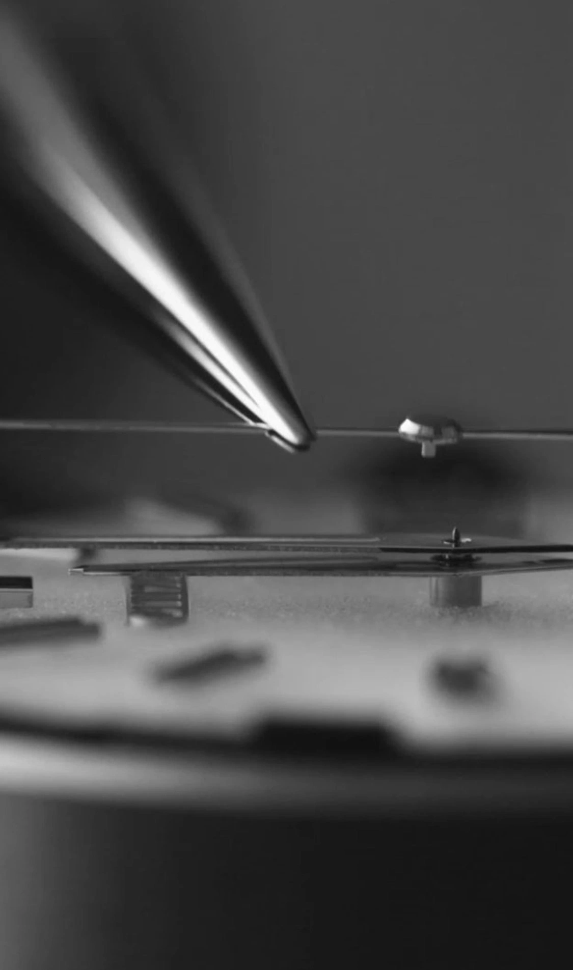 Close-up van horlogemechanisme met gereedschap, zwart-wit, gedetailleerd.