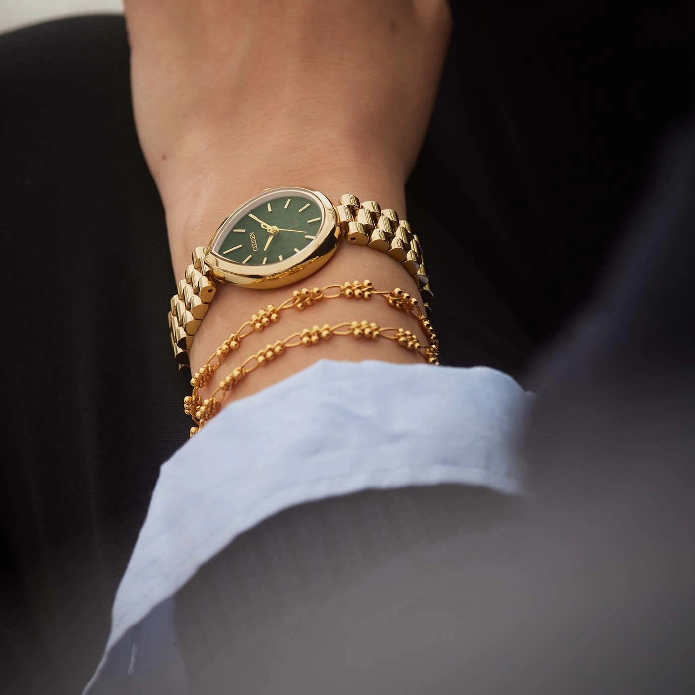 Een gouden horloge en armbanden om de pols van een vrouw