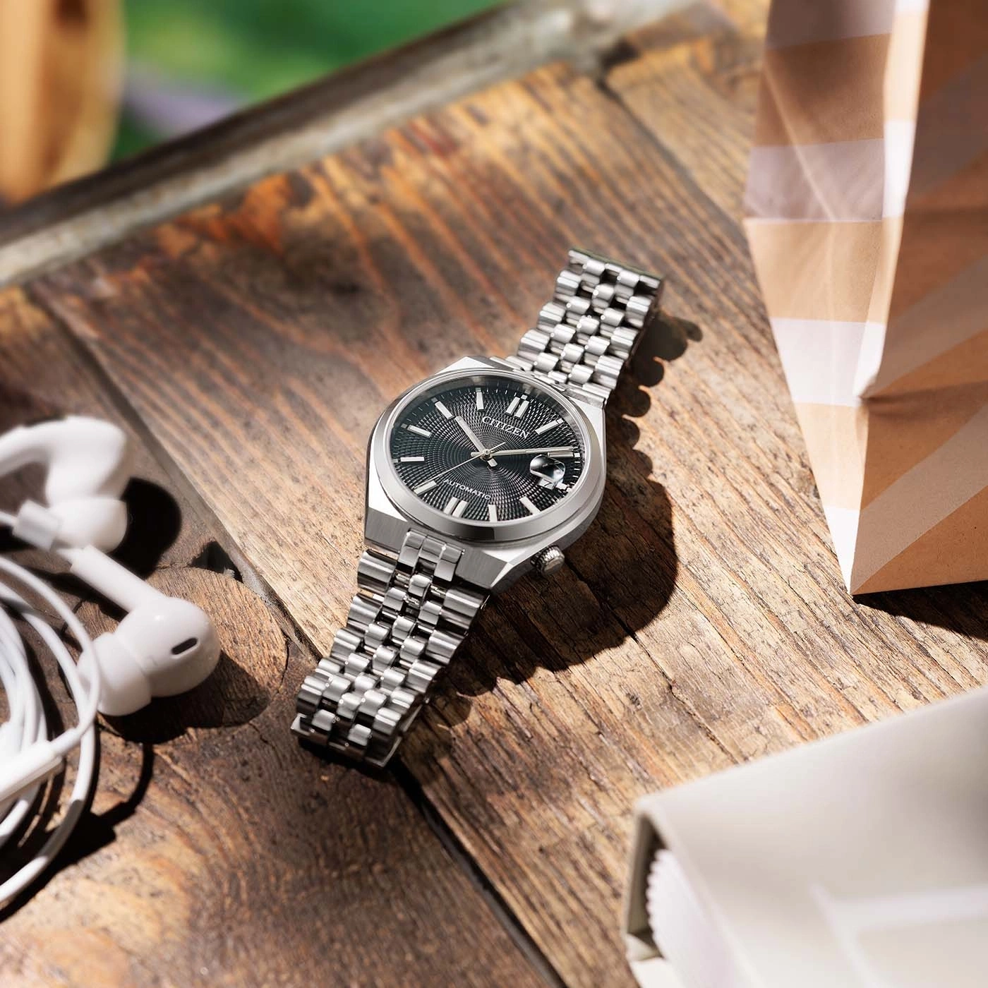 Een close-up van een Citizen horloge op een houten tafel met oordopjes.