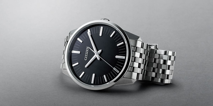 Citizen horloge met zwarte wijzerplaat en zilveren band op grijze ondergrond