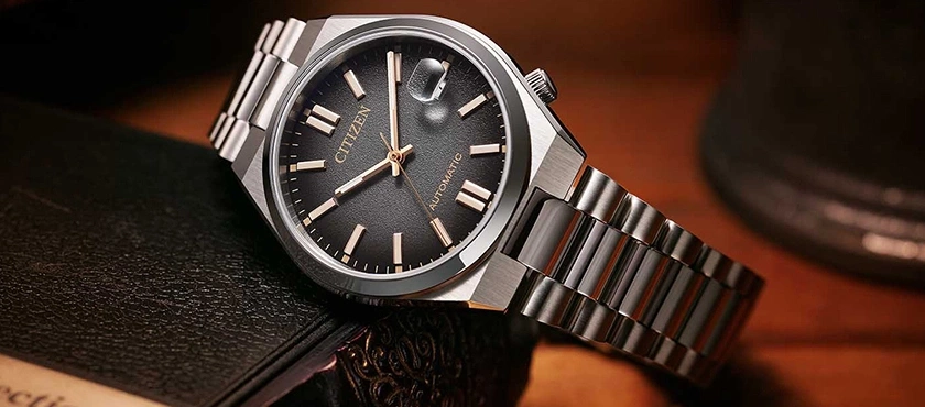 Citizen horloge met zwarte wijzerplaat en zilveren armband op een boek
