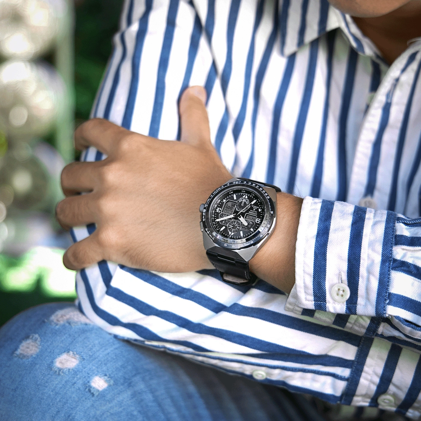Man met horloge, blauw-wit gestreept overhemd en gescheurde jeans.