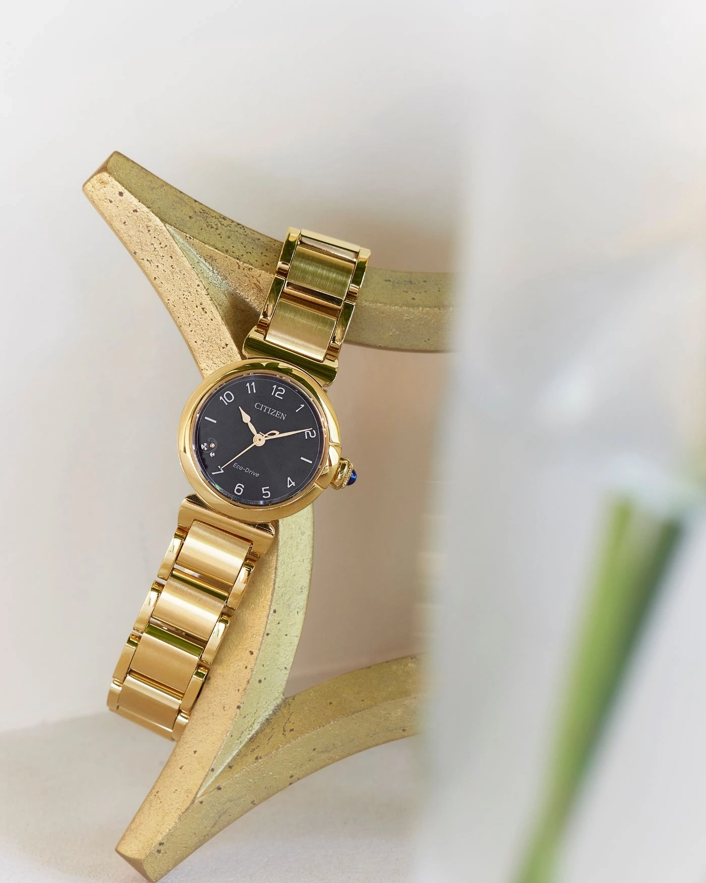 Gouden Citizen horloge op een gouden standaard met een zwarte wijzerplaat en gouden band.
