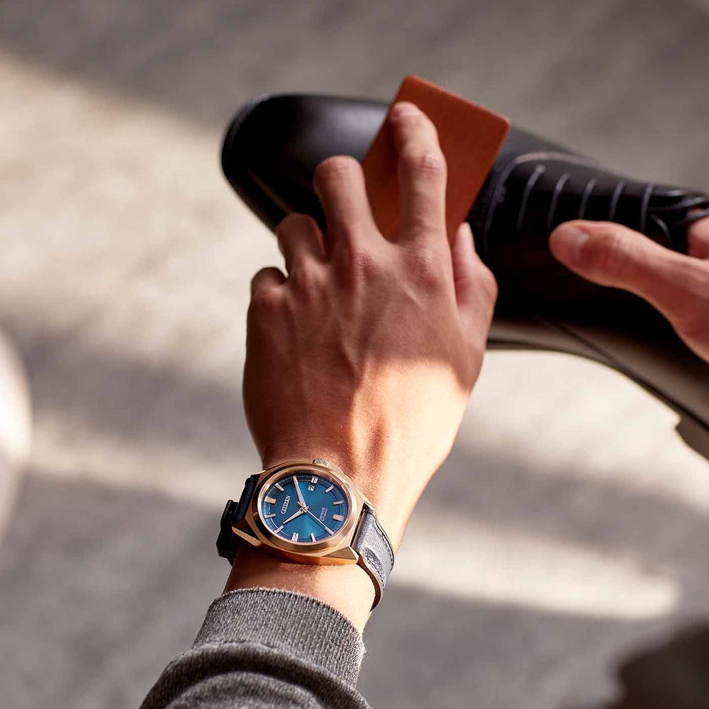 Man die een zwarte schoen oppoetst, draagt een gouden horloge met blauwe wijzerplaat.