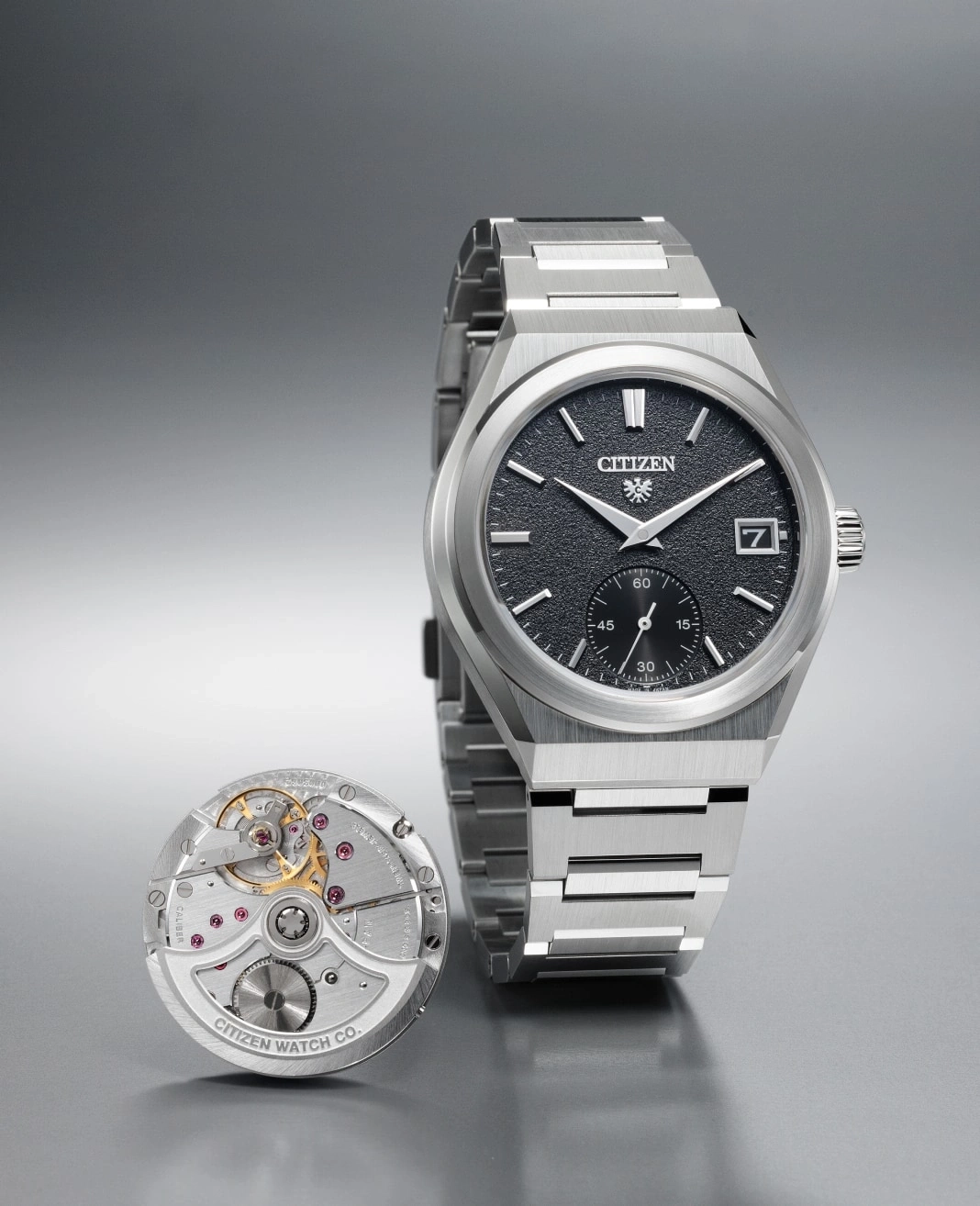 Citizen horloge met blootliggend mechanisme en roestvrijstalen armband op grijze ondergrond.