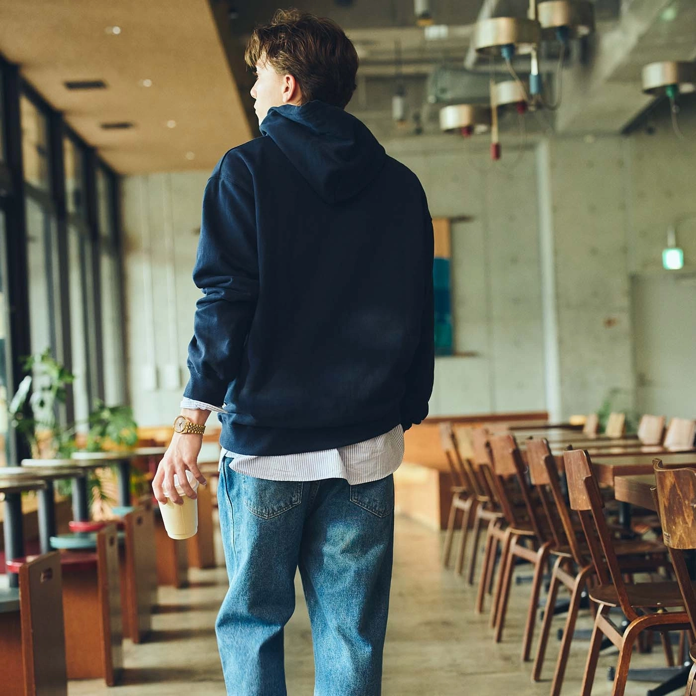 Man in hoodie en spijkerbroek houdt een koffiebeker vast in een café