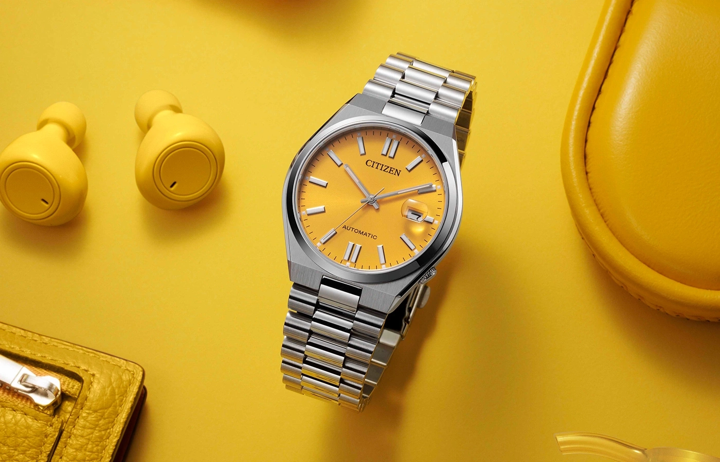 Citizen horloge, gele achtergrond, oortelefoons, portemonnee en een gele tas.