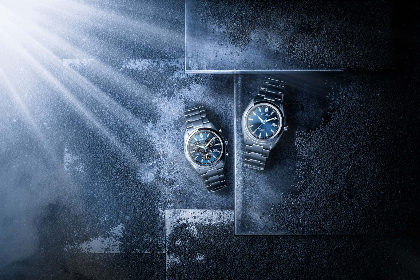 Twee Citizen Eco-Drive titanium horloges op donker gestructureerd oppervlak met lichtstralen.