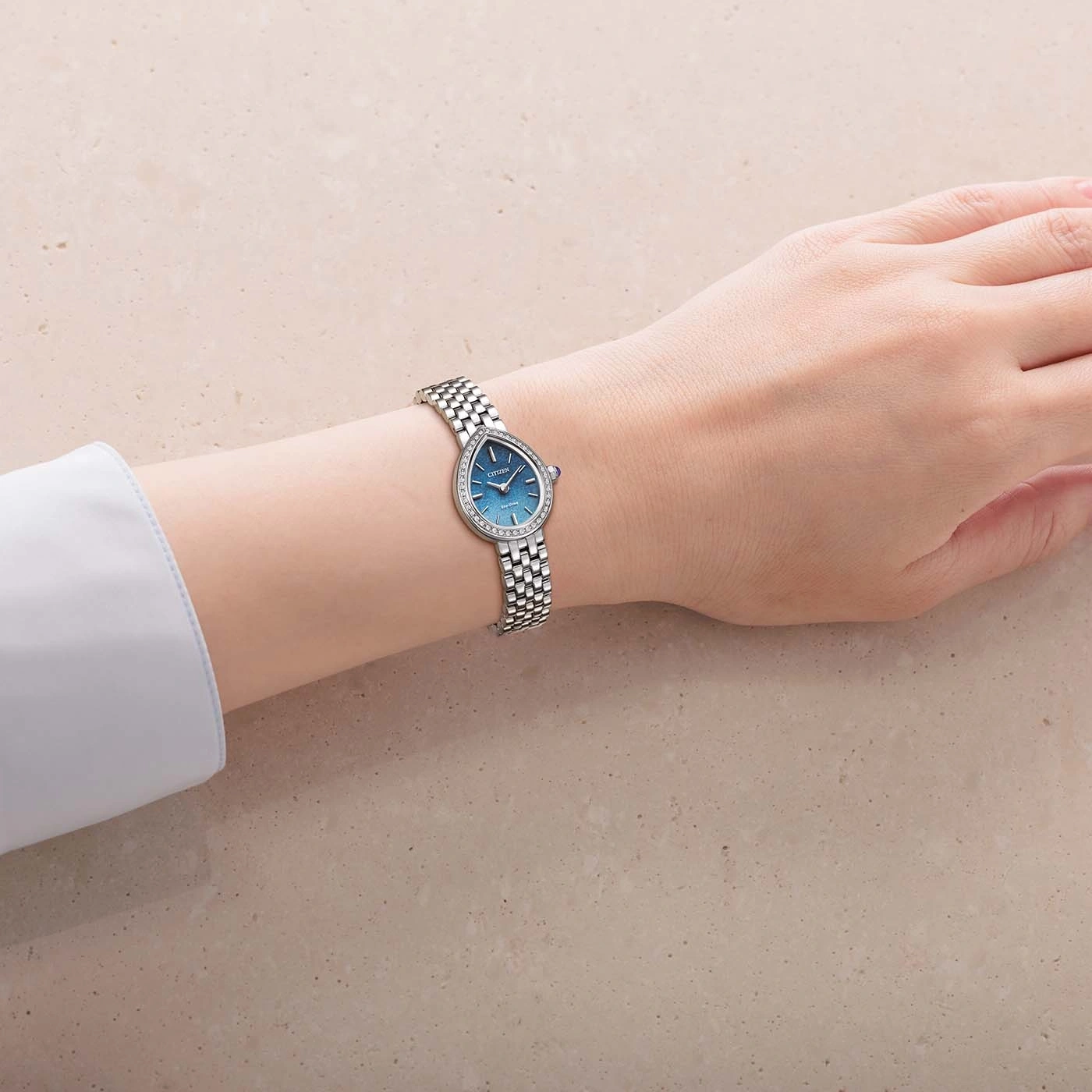 Pols van een vrouw met een druppelvormig horloge met diamantaccenten.