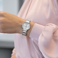 De pols van een vrouw met een zilveren horloge met een witte wijzerplaat en Romeinse cijfers.