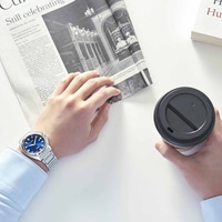 Man houdt krant en koffie vast, draagt een horloge.