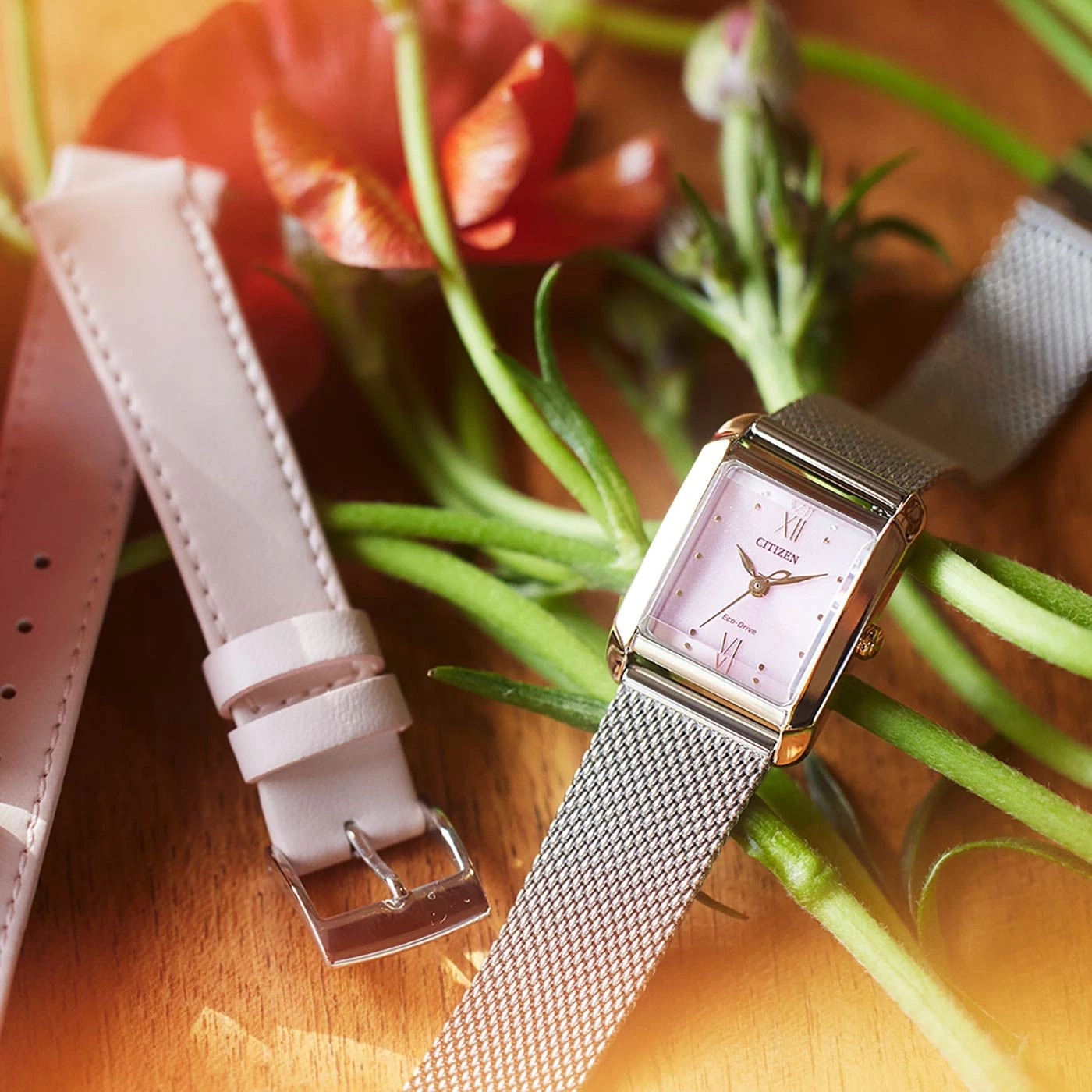 Citizen horloge met roze wijzerplaat en mesh band, met een reserve leren band en bloemen.