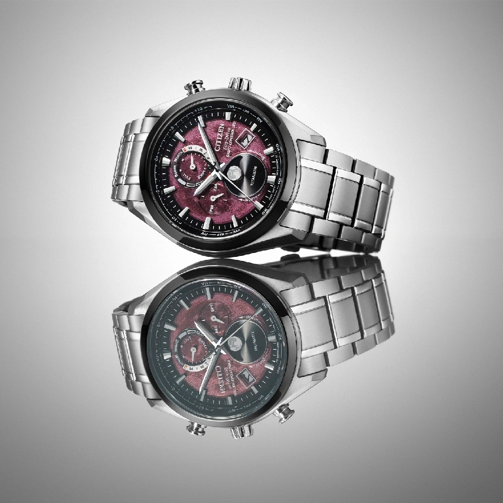 Citizen horloge met rode wijzerplaat en titanium band, weerspiegeld op een oppervlak.