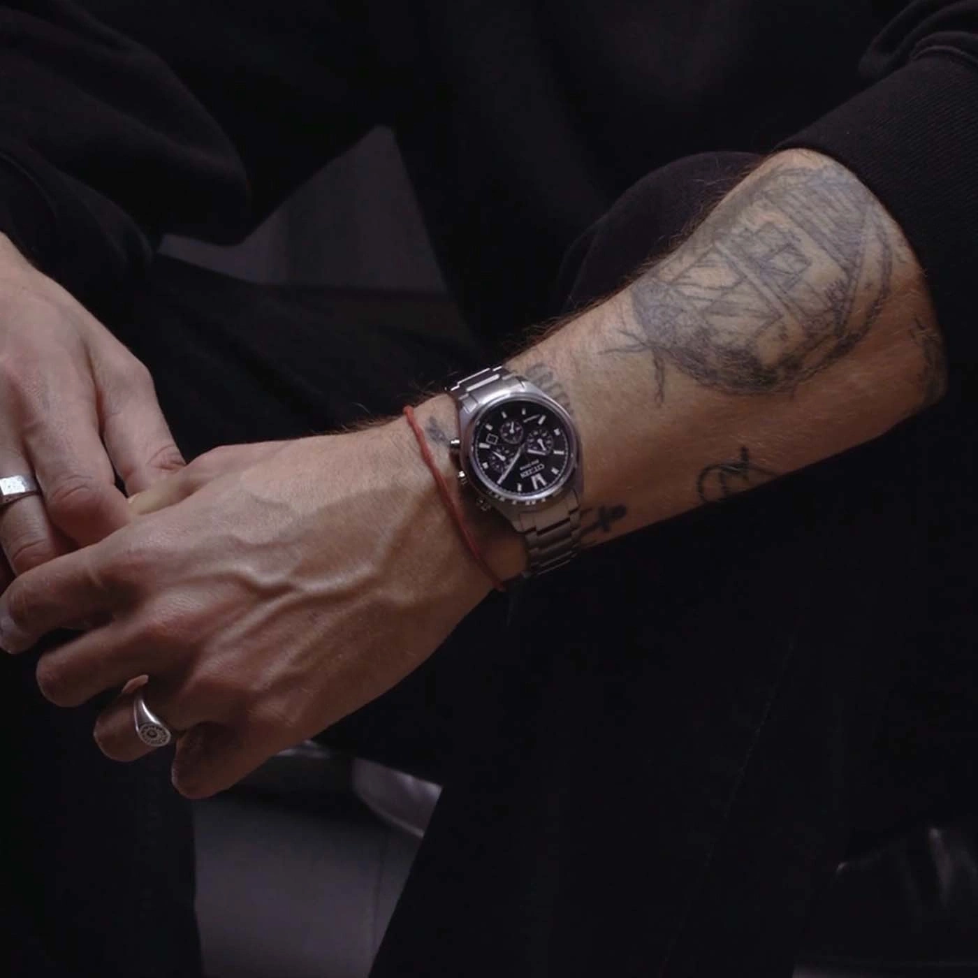Close-up van een getatoeëerde arm van een man met een horloge en ringen.