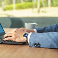 Man met horloge, typt op laptop, met een kopje koffie op tafel.