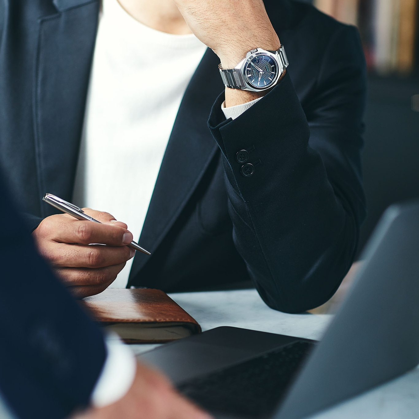Man in pak met horloge en pen, werkend op laptop, zakelijke bijeenkomst.