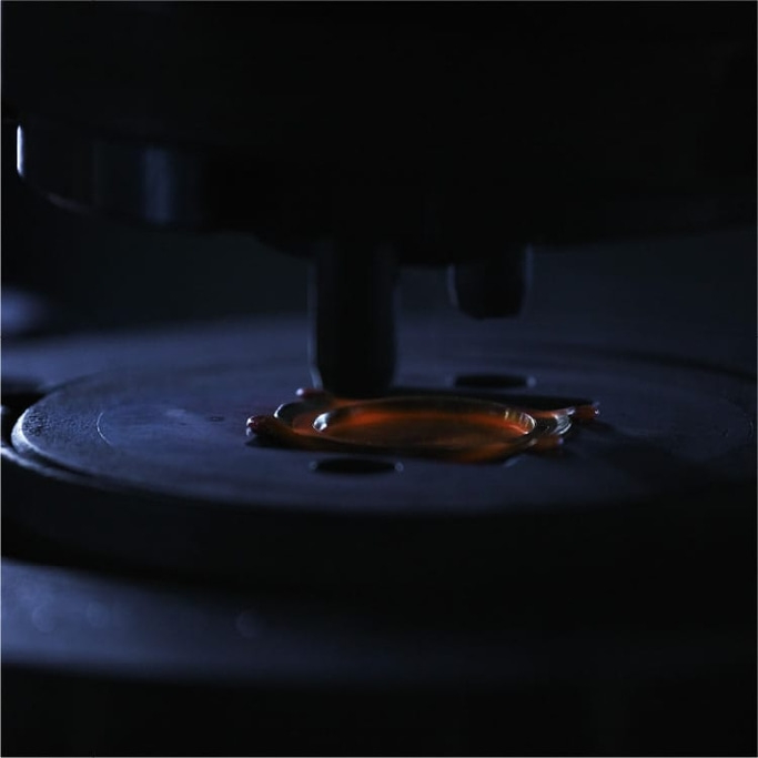 Close-up van een donkere machine met een druppel oranje vloeistof op een plaat.