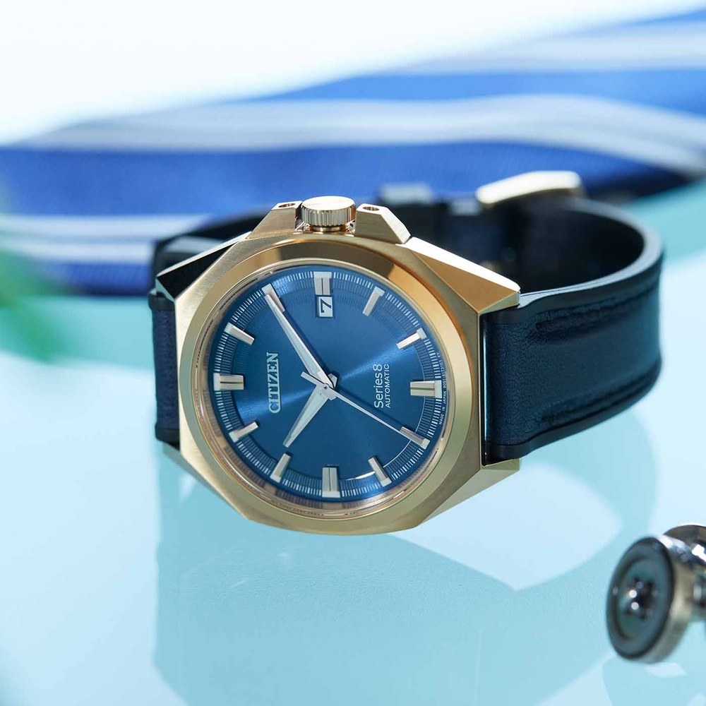 Citizen horloge met blauwe wijzerplaat en gouden kast op blauwe ondergrond.