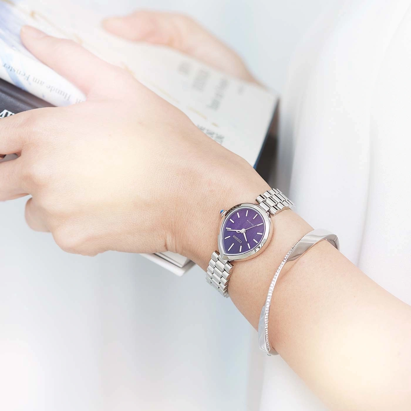 Vrouw met paarse horloge en zilveren armband, aan het lezen.