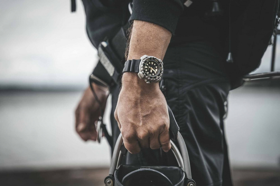 Man met horloge, houdt apparatuur vast, close-up, zwarte outfit, buiten