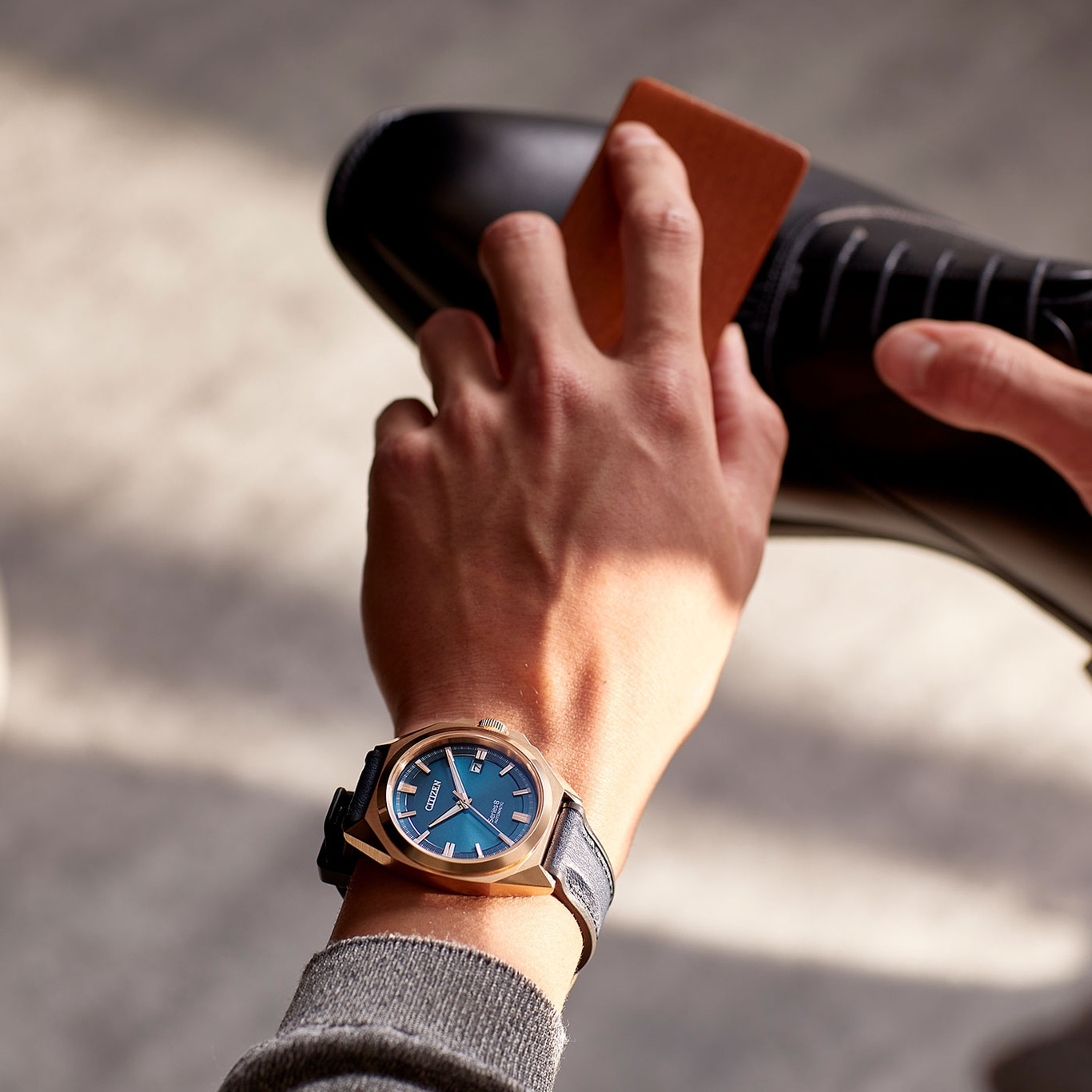 Man poetst zwarte schoen, draagt gouden horloge met blauwe wijzerplaat.