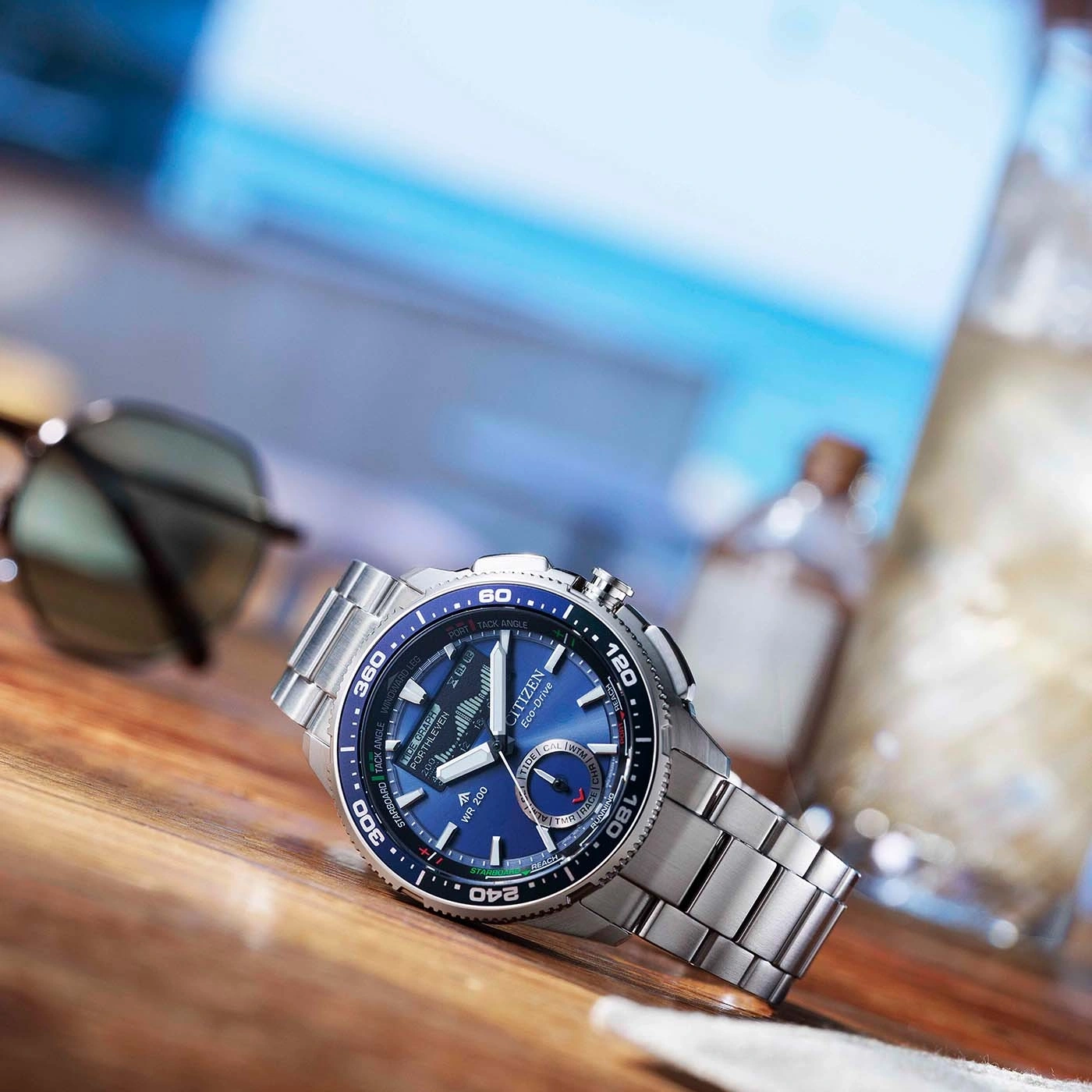 Een blauw Citizen Eco-Drive horloge op een houten tafel met zonnebril.