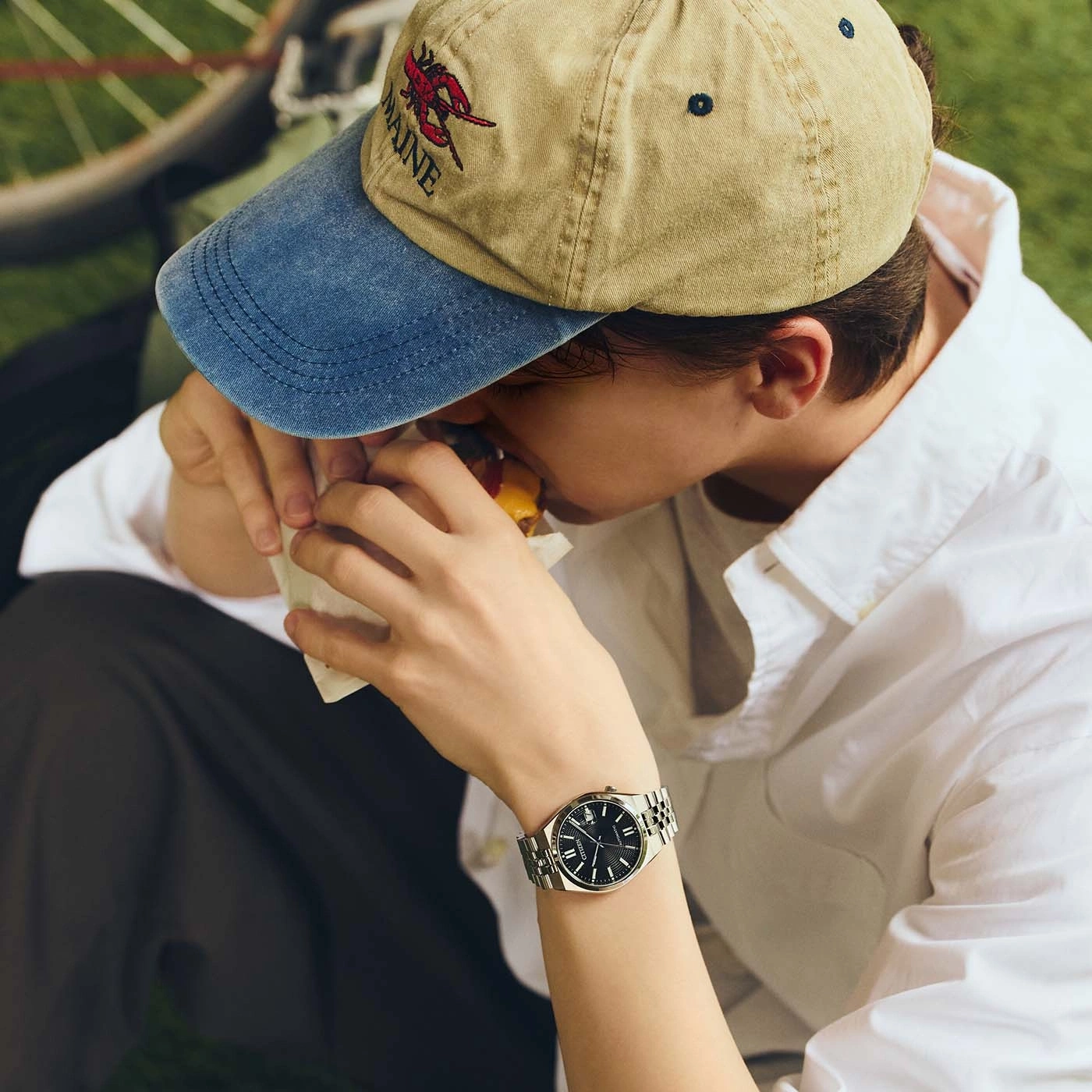 Een persoon eet een hamburger met een pet en een horloge