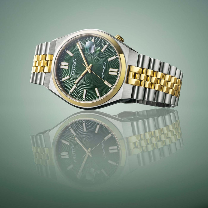 Citizen horloge met groene wijzerplaat en gouden en zilveren band, weerspiegeld.