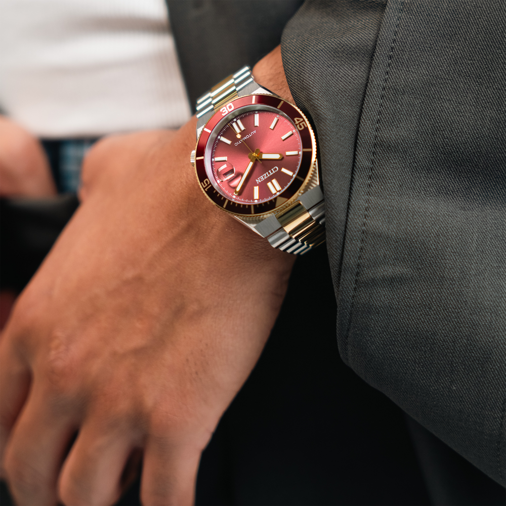 Een man draagt een rood Citizen automatisch horloge om zijn pols, met een grijs pak.