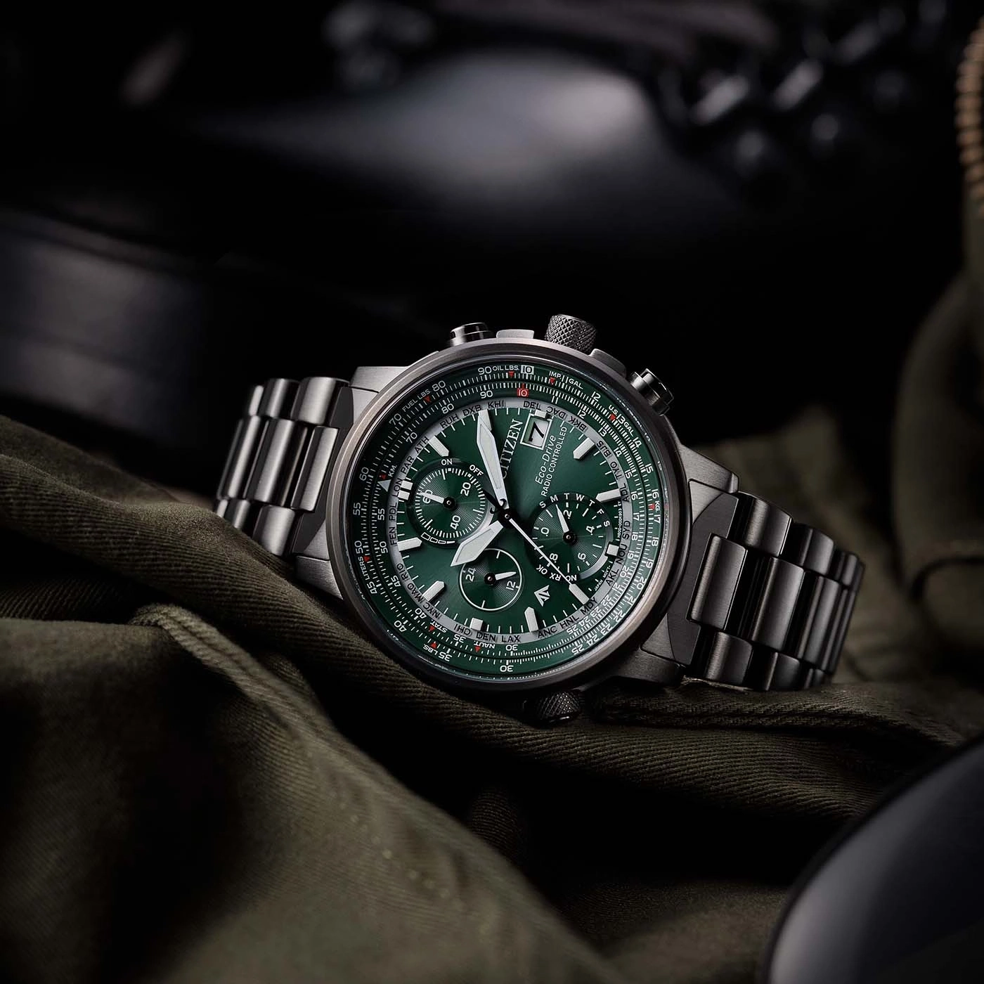 Citizen horloge met groene wijzerplaat en metalen band op groene stoffen achtergrond.