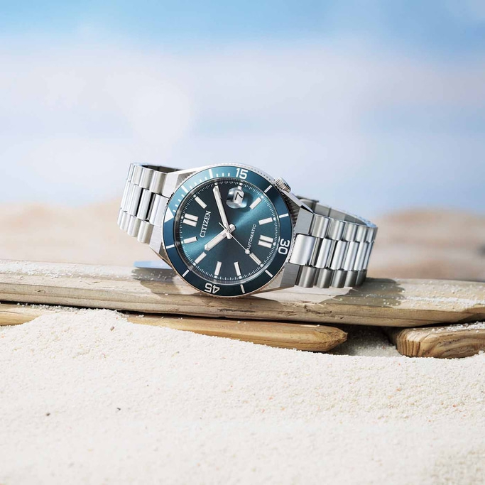 Een Citizen automatisch horloge rust op drijfhout op een zandstrand.